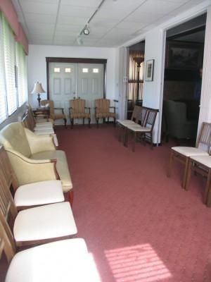 A waiting room with chairs, a couch, and a door, all on a red carpet.