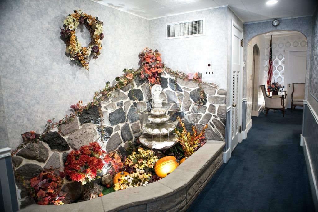 Fountain with stone wall and floral arrangements in a hallway. A wreath hangs above.