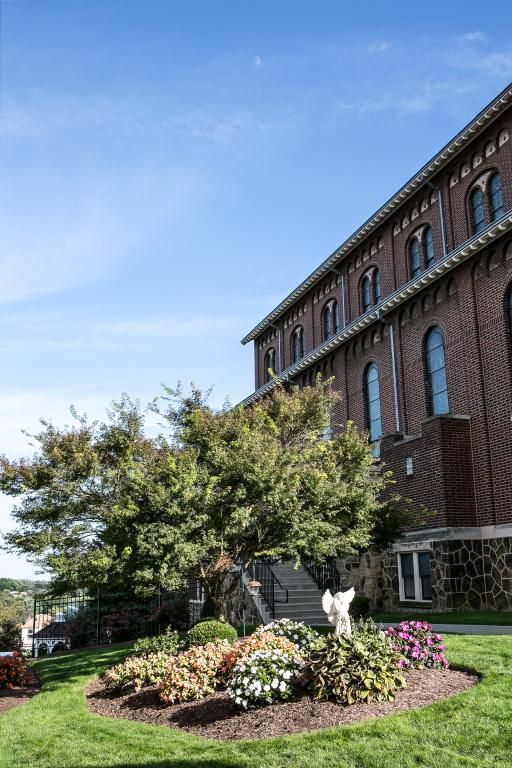 Brick building with arched windows, next to a landscaped garden, under a blue sky.
