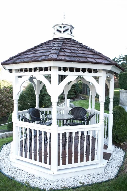 White gazebo with brown roof, containing table and chairs, set on white stones.