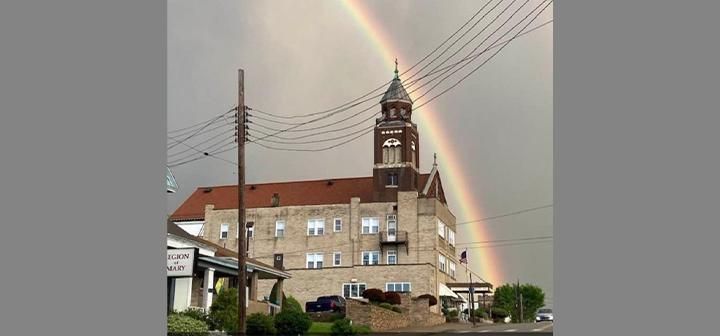 A building with a clock tower and a rainbow arching above it.