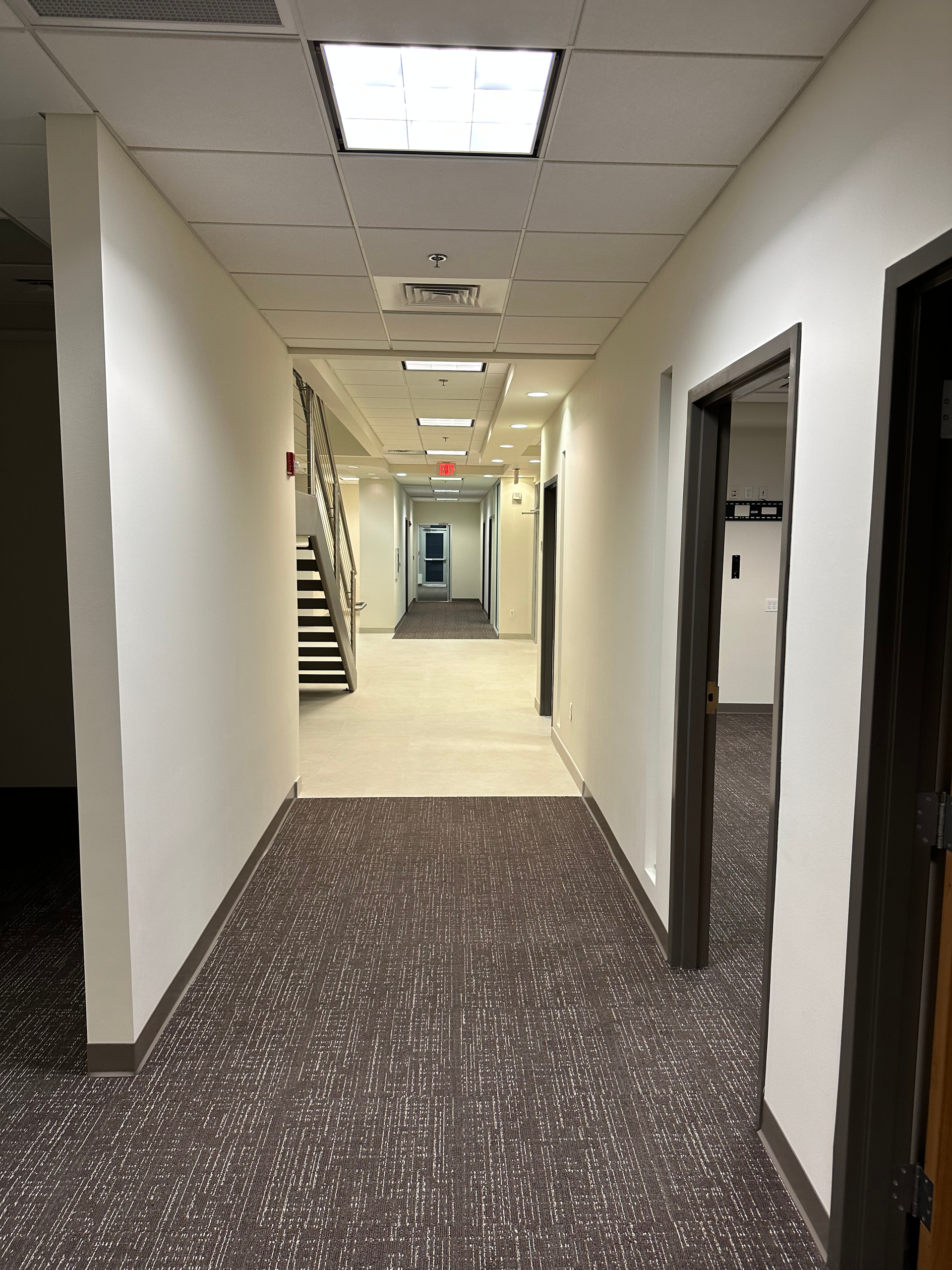 A long hallway with stairs and doors in a building.