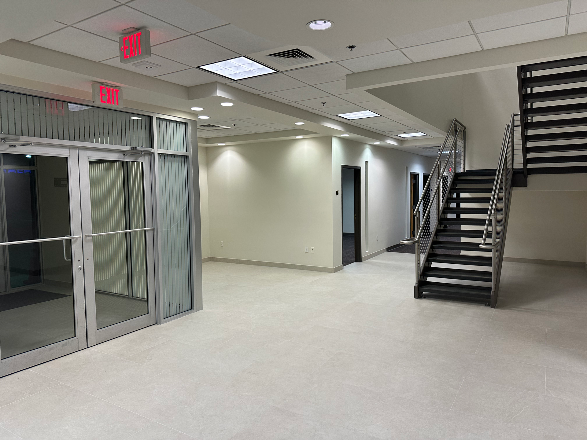 An empty room with stairs and a red exit sign
