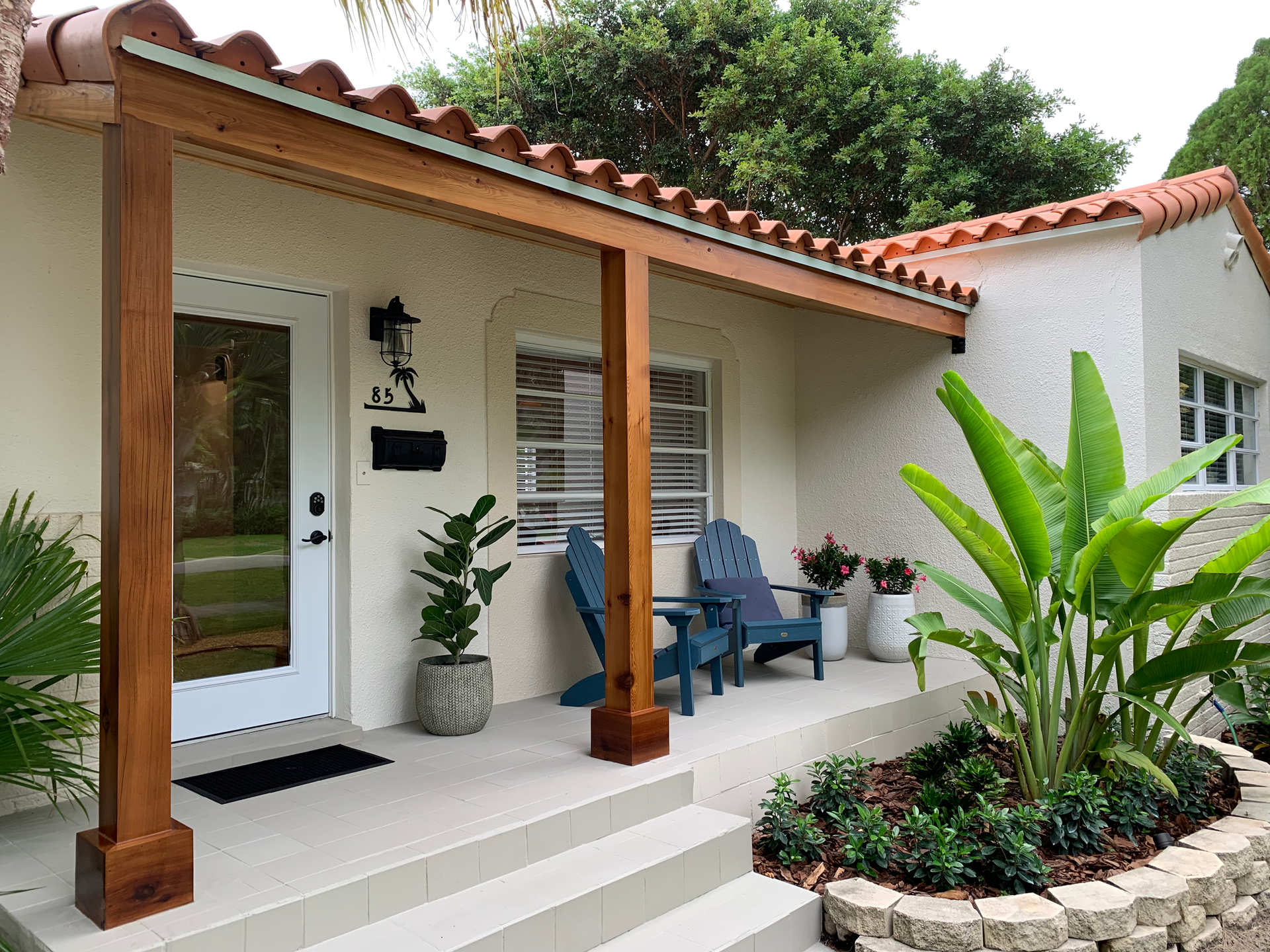 A white house with a wooden porch and chairs on it.