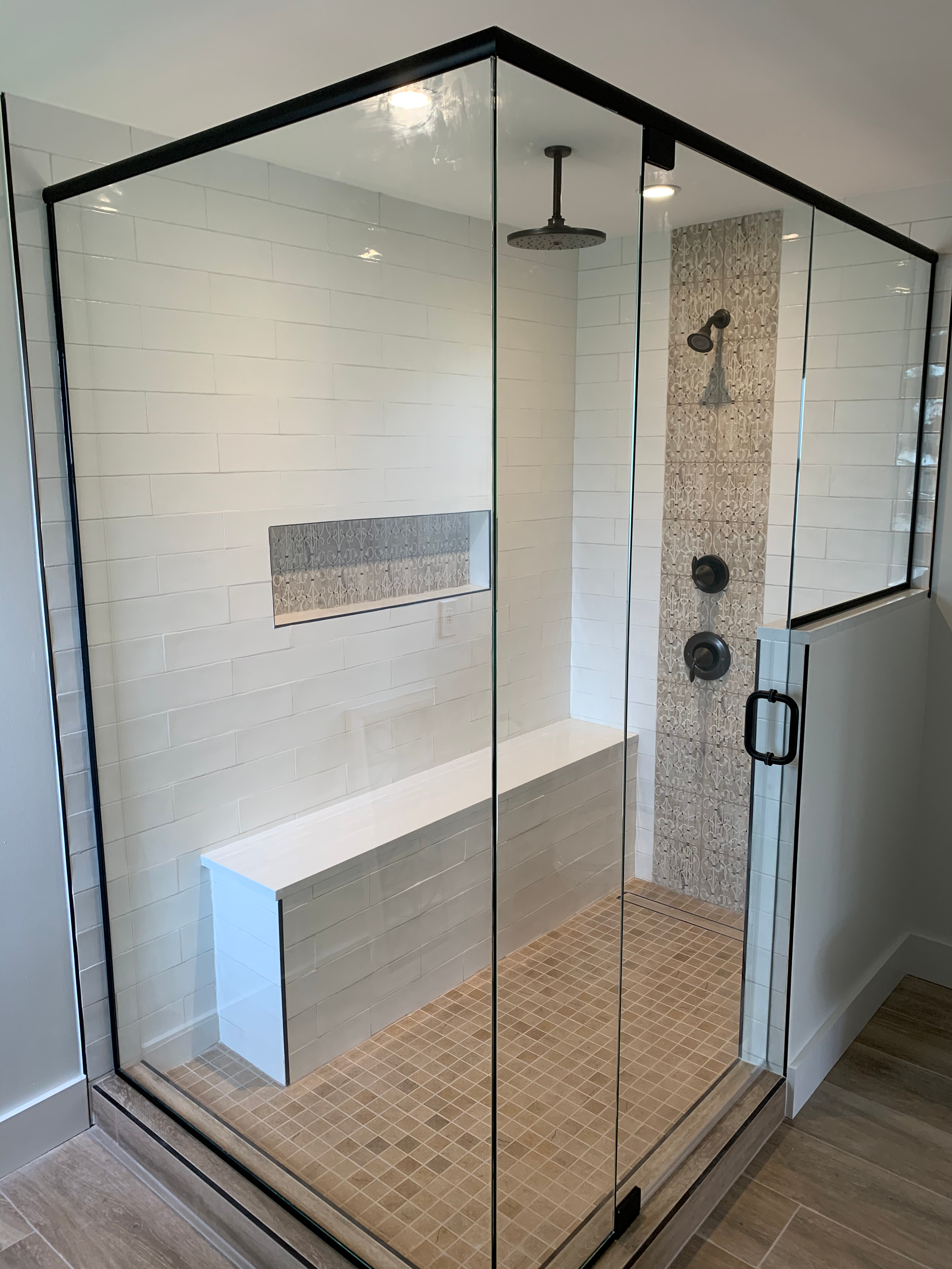 A bathroom with a walk in shower with a glass door and a bench.