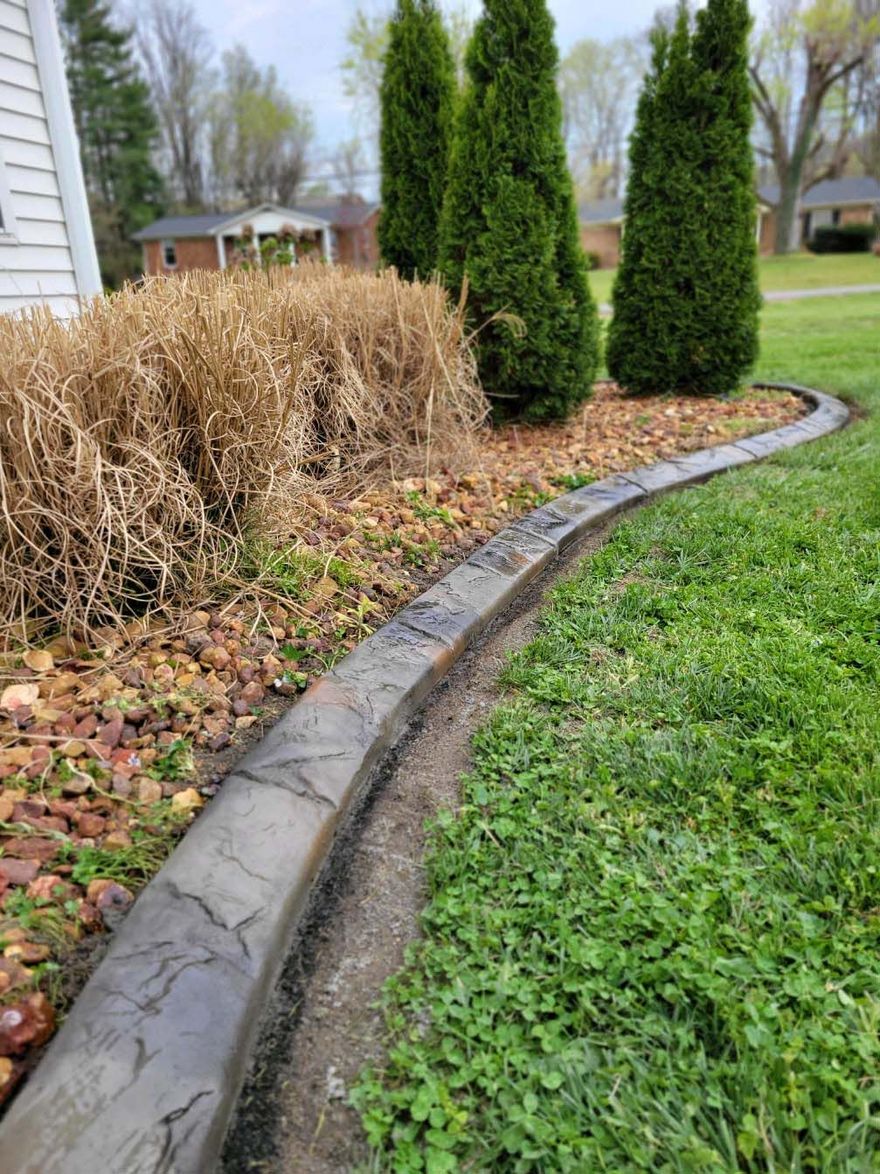 A concrete curb is surrounded by grass and trees in a yard.