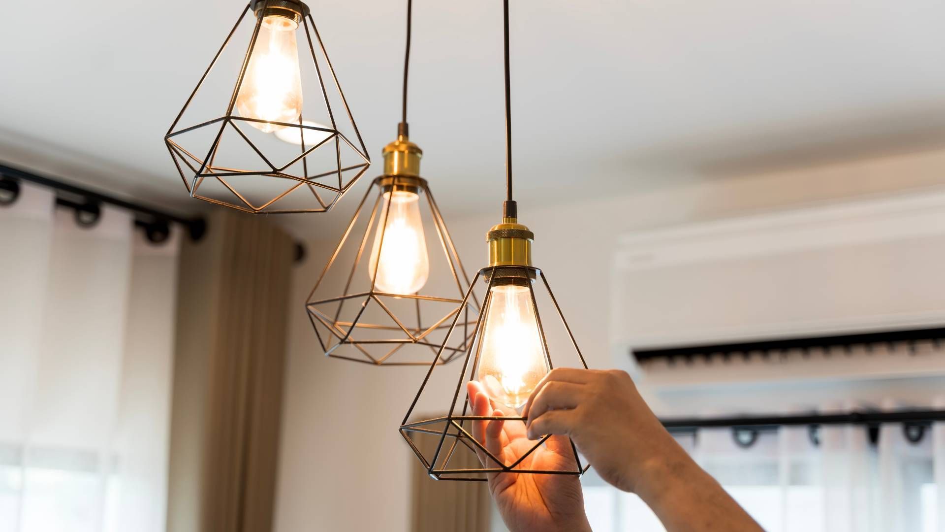Person replaces lightbulb in pendant lamp fixture with geometric cage design.