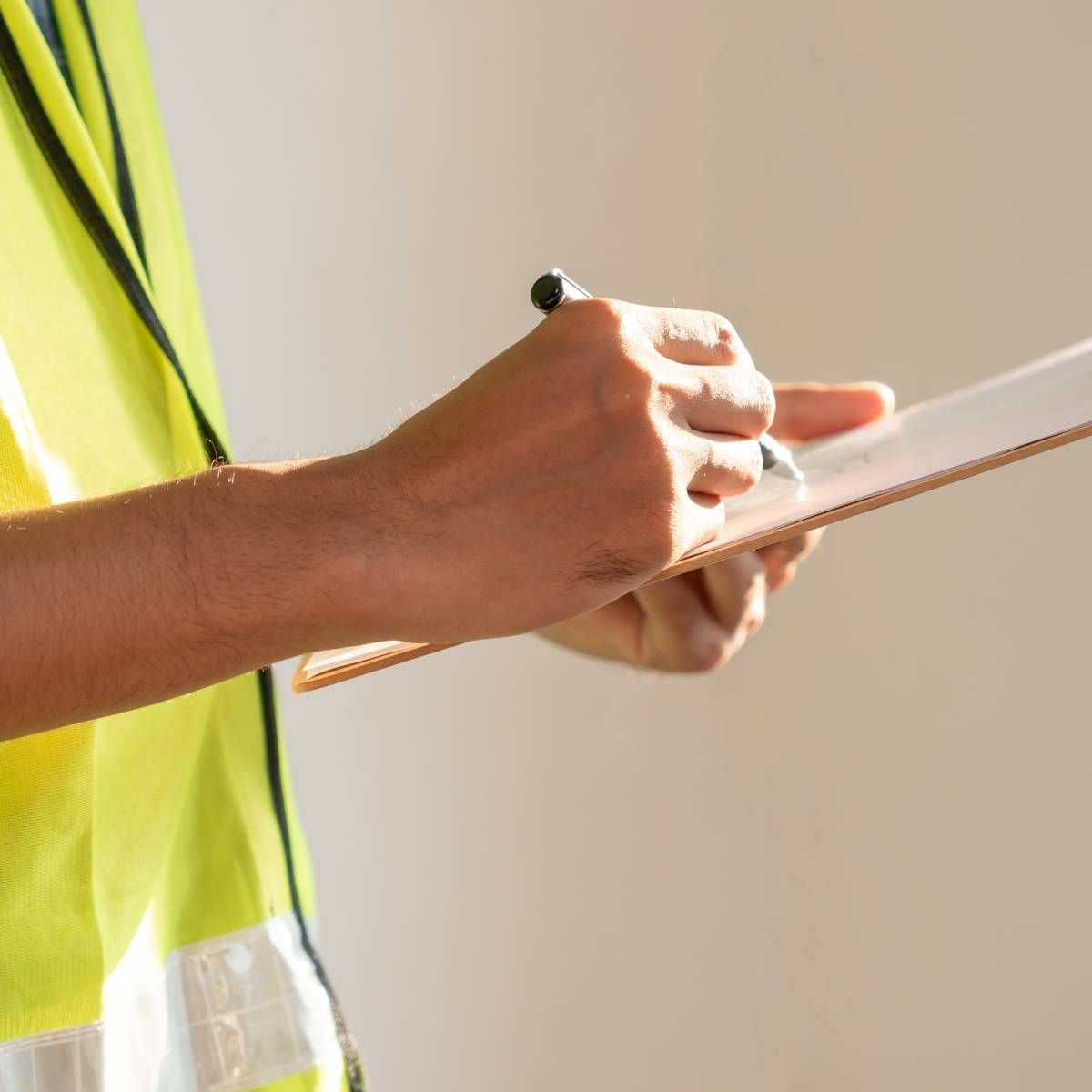 Person in yellow safety vest writing on a clipboard.