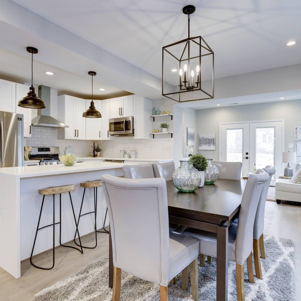 Modern kitchen and dining room with white cabinets, island with stools, and dark wooden table with upholstered chairs.