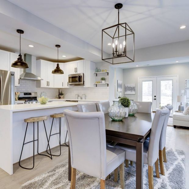 Modern kitchen and dining room with white cabinets, island with stools, and dark wooden table with upholstered chairs.