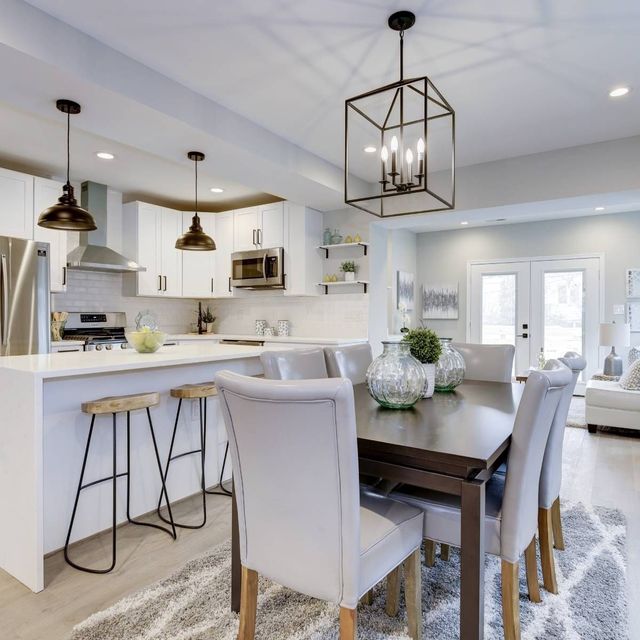 Modern kitchen and dining room with white cabinets, island with stools, and dark wooden table with upholstered chairs.