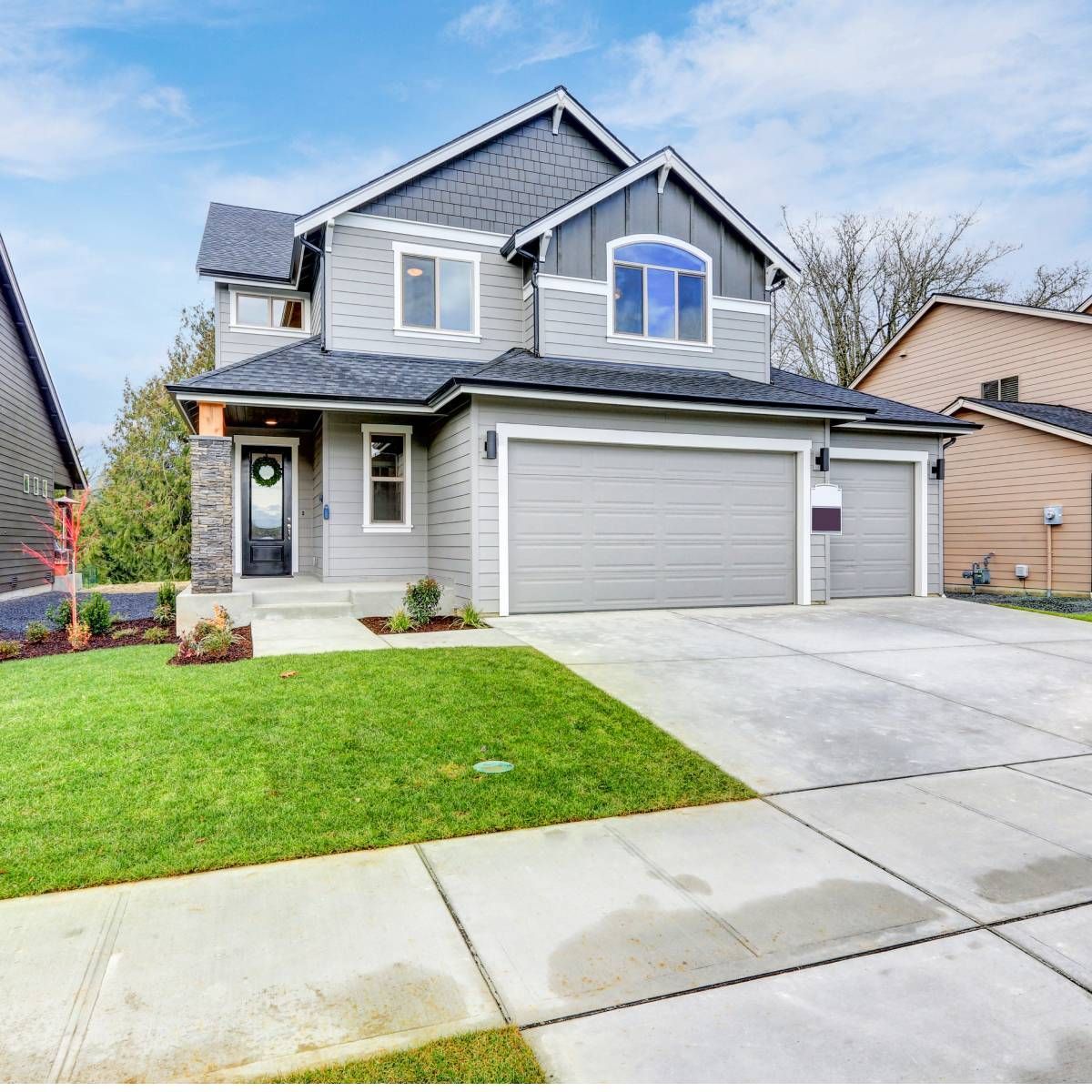 Gray two-story house with a two-car garage, green lawn, and concrete driveway on a sunny day.