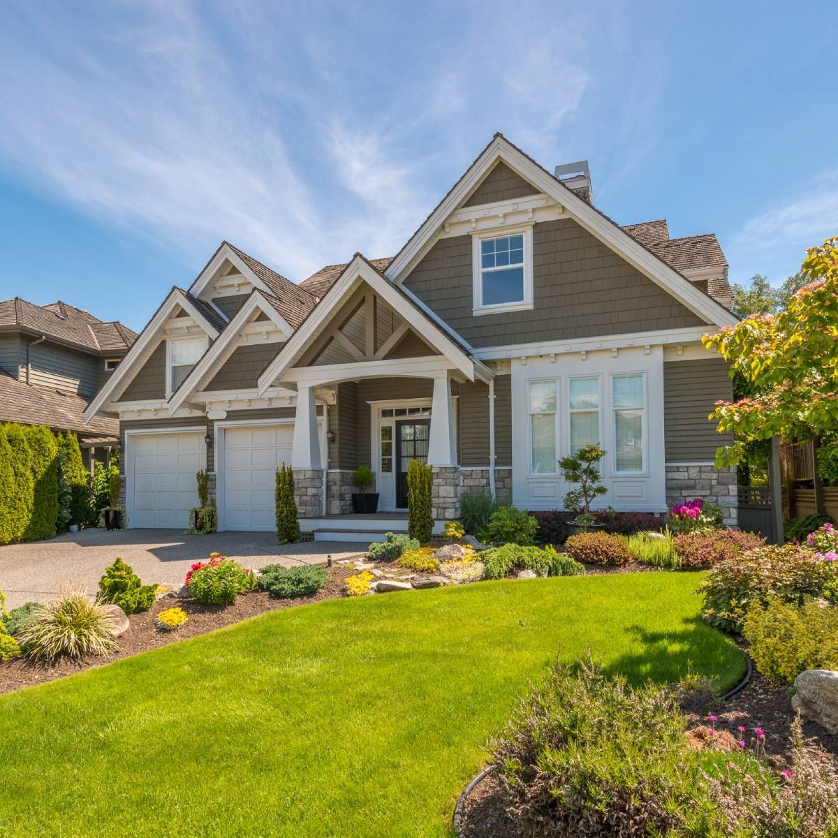 Green-sided house with white trim, three-car garage, lush lawn, and colorful garden under a blue sky.