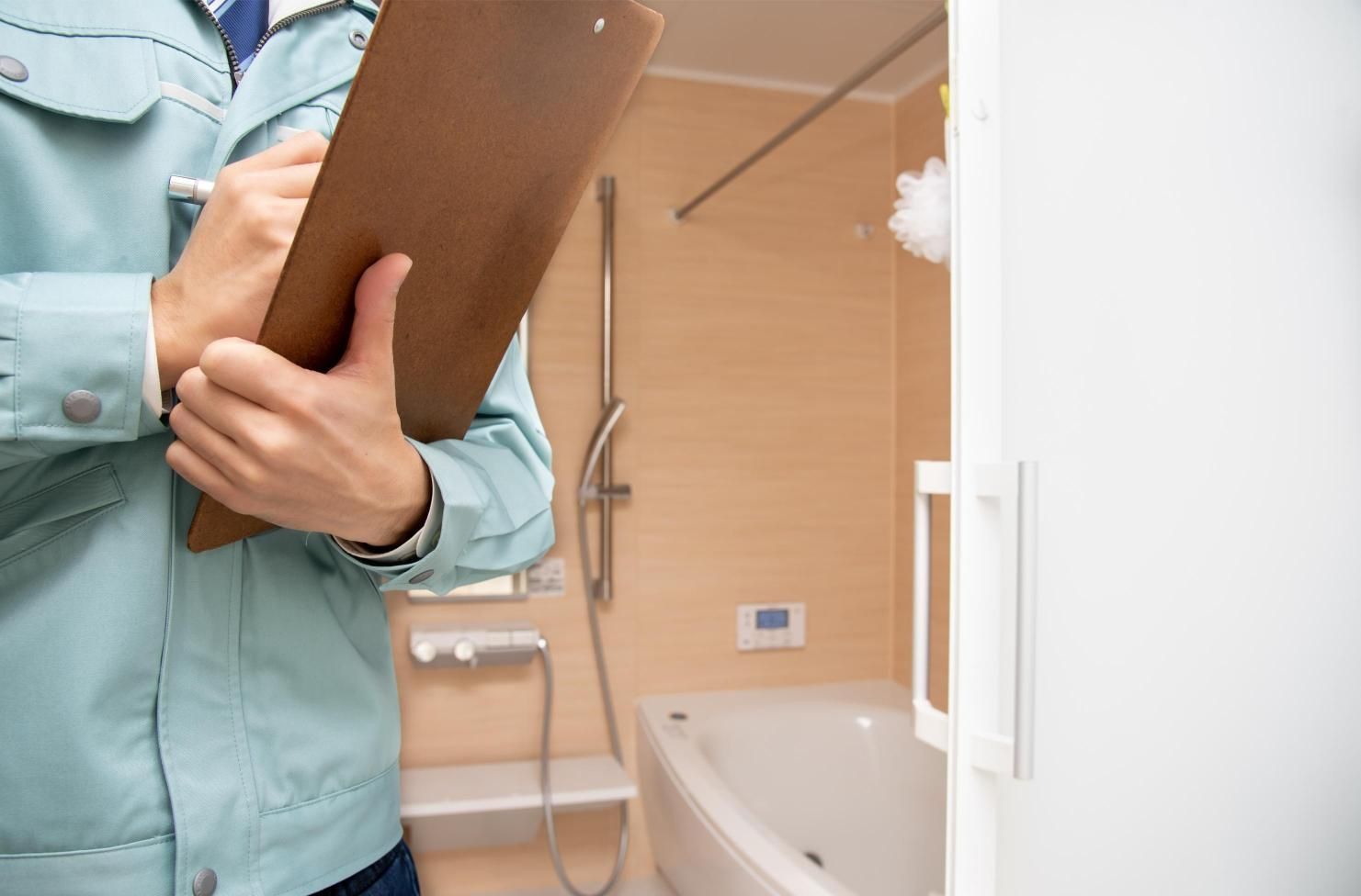 Person in light blue jacket with clipboard in hand inspecting a bathroom.