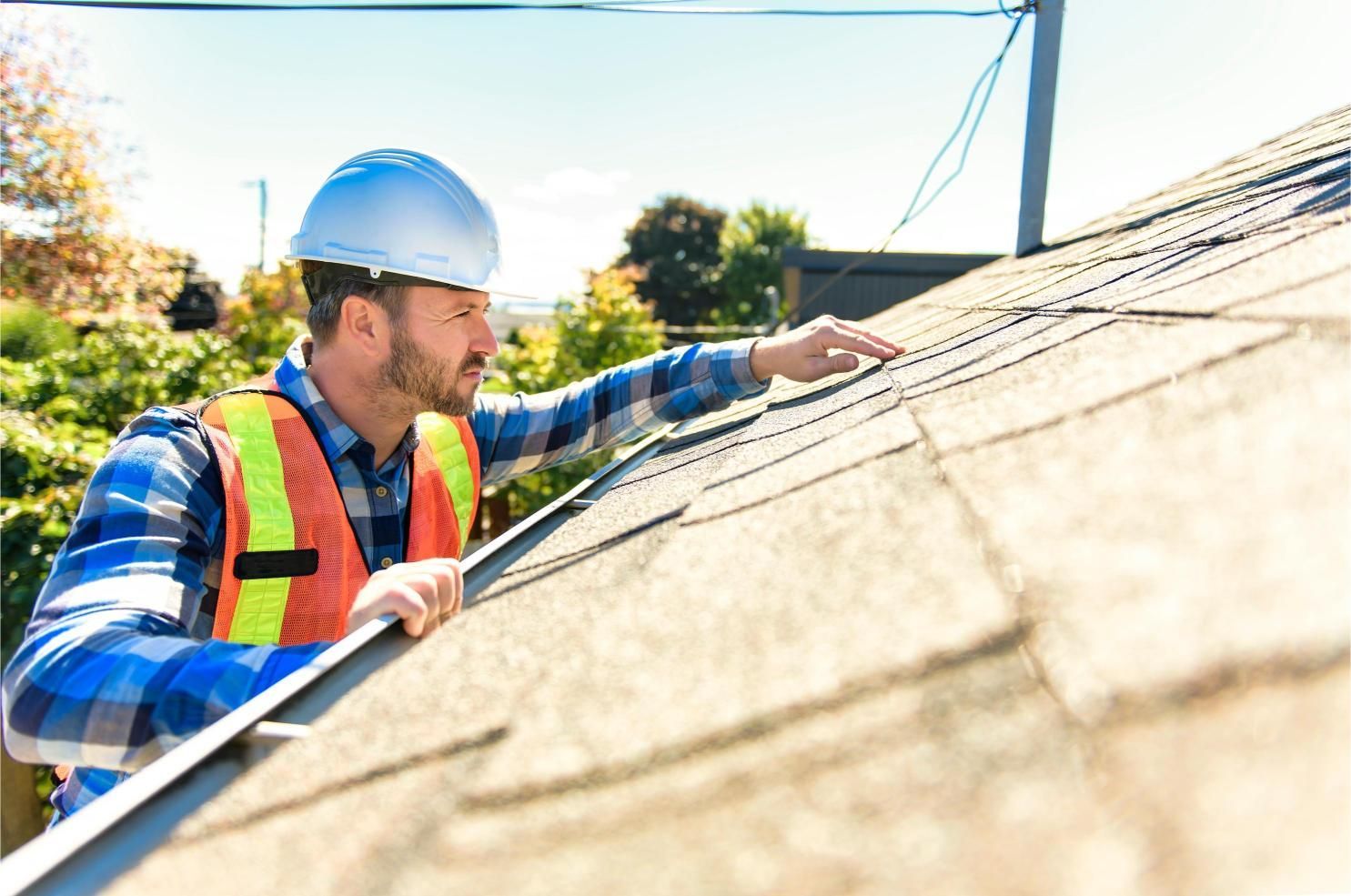 A person in a hard hat and safety vest examines a rooftop.