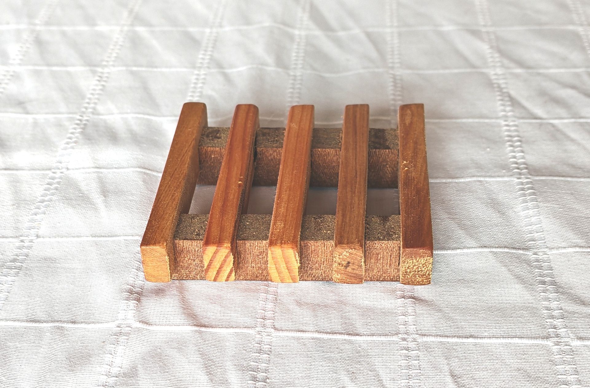 Una jabonera de madera reposa sobre una manta blanca.