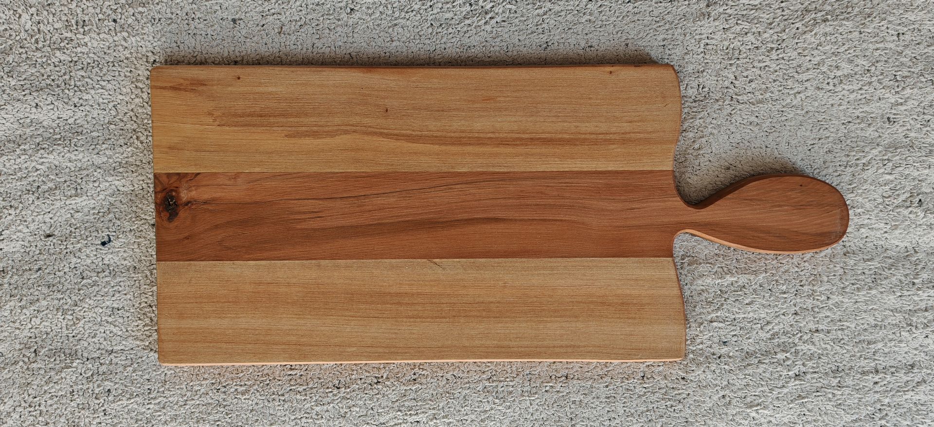 Una tabla de cortar de madera con mango está colocada sobre un mostrador.