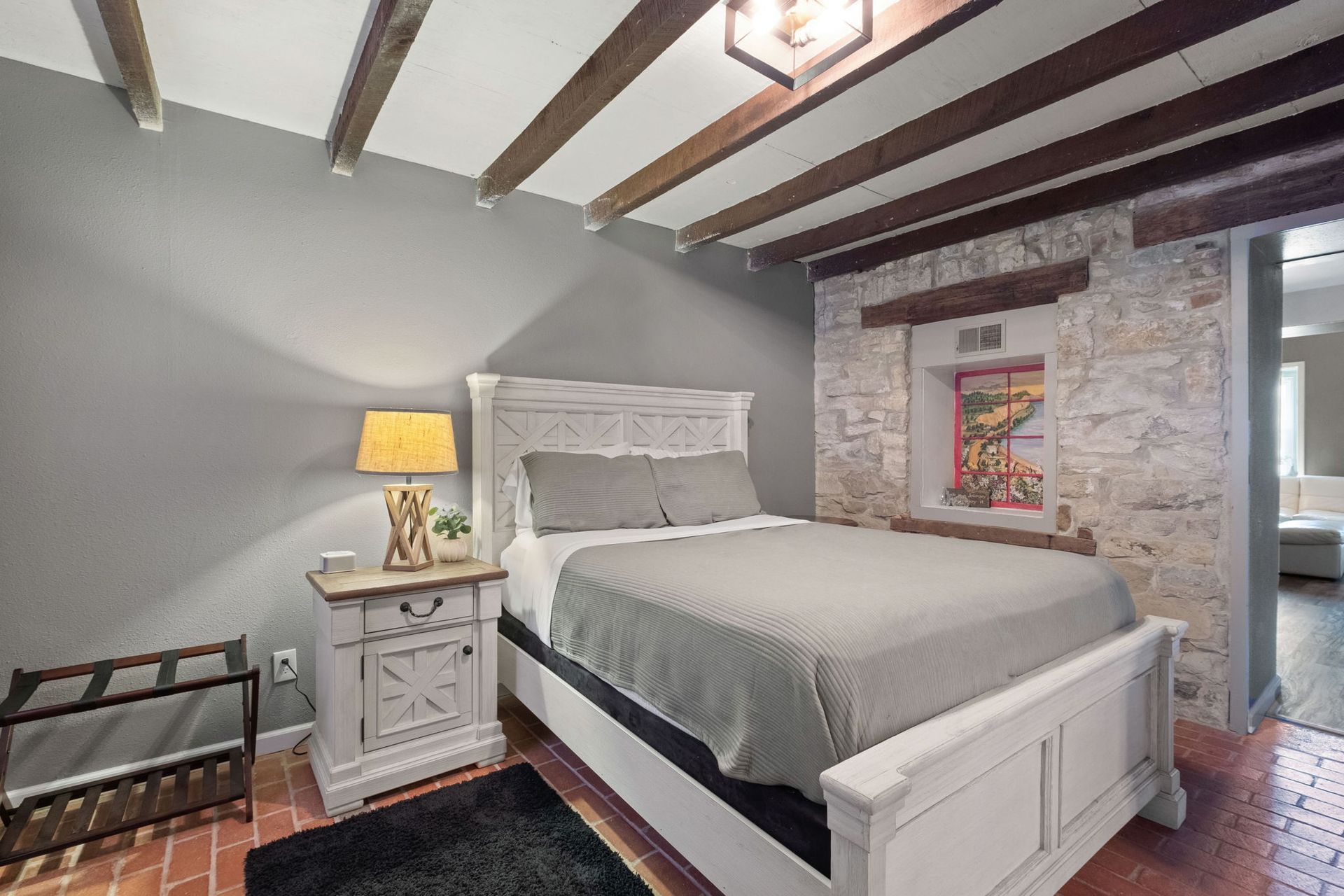 A bedroom with a bed , nightstand , lamp and stone wall.