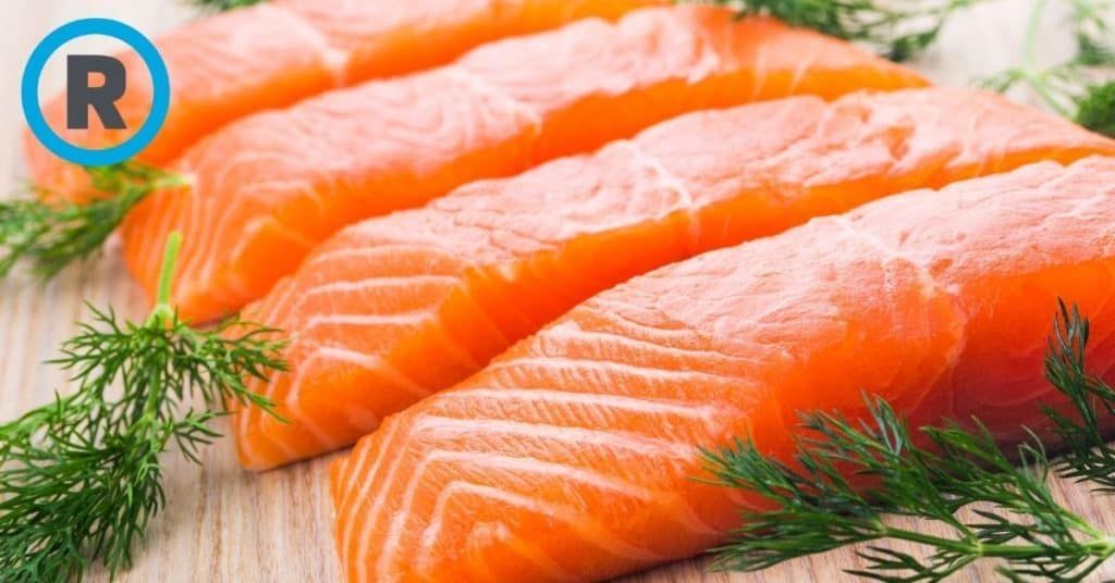 A close up of salmon with dill on a wooden table.