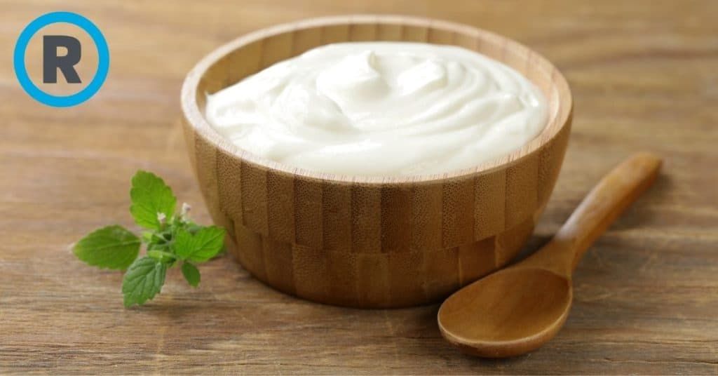 A wooden bowl filled with yogurt and a wooden spoon on a wooden table.