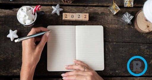 A person is writing in a notebook on a wooden table.