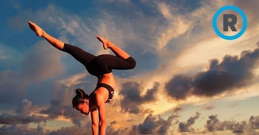 A woman is doing a handstand in front of a cloudy sky.