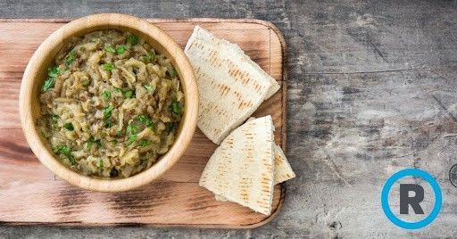 A bowl of food and pita bread on a wooden cutting board.