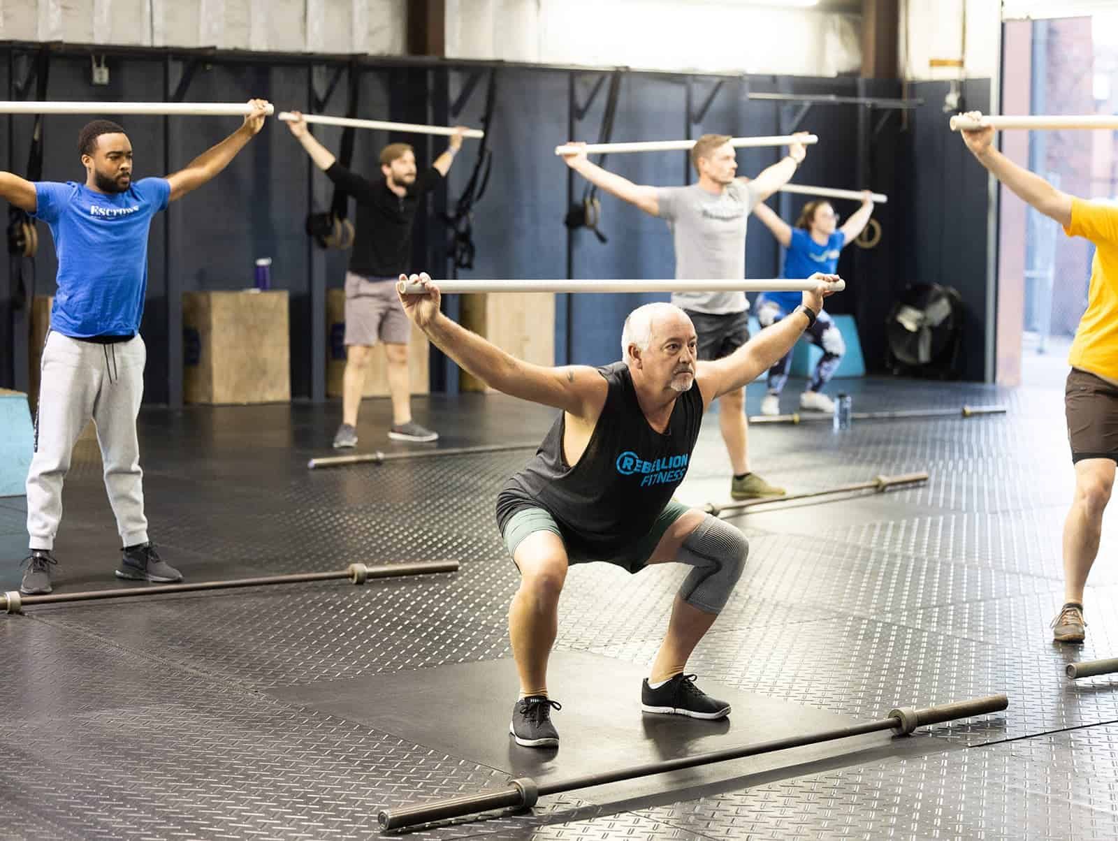 A group of people are doing squats with barbells in a gym.