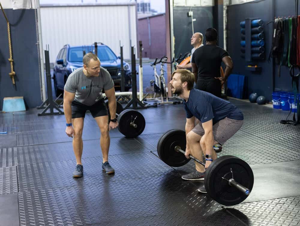 A man is squatting down to lift a barbell in a gym.