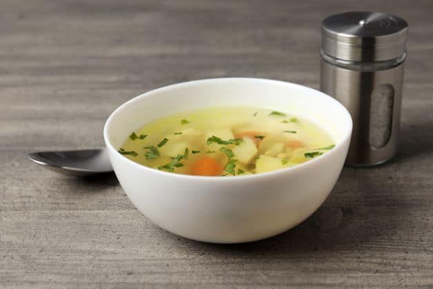 A bowl of soup with potatoes and carrots next to a spoon.