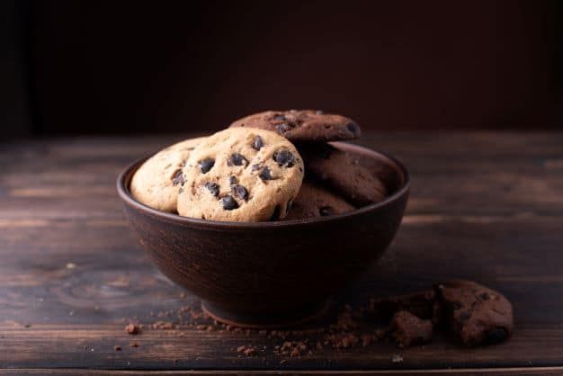 A bowl filled with chocolate chip cookies on a wooden table.