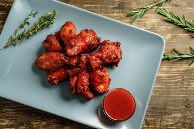 A plate of chicken wings with a dipping sauce on a wooden table.