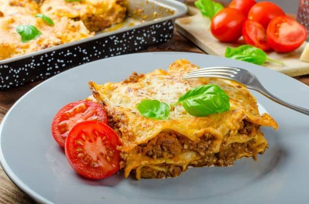 A slice of lasagna with tomatoes and basil on a plate with a fork.