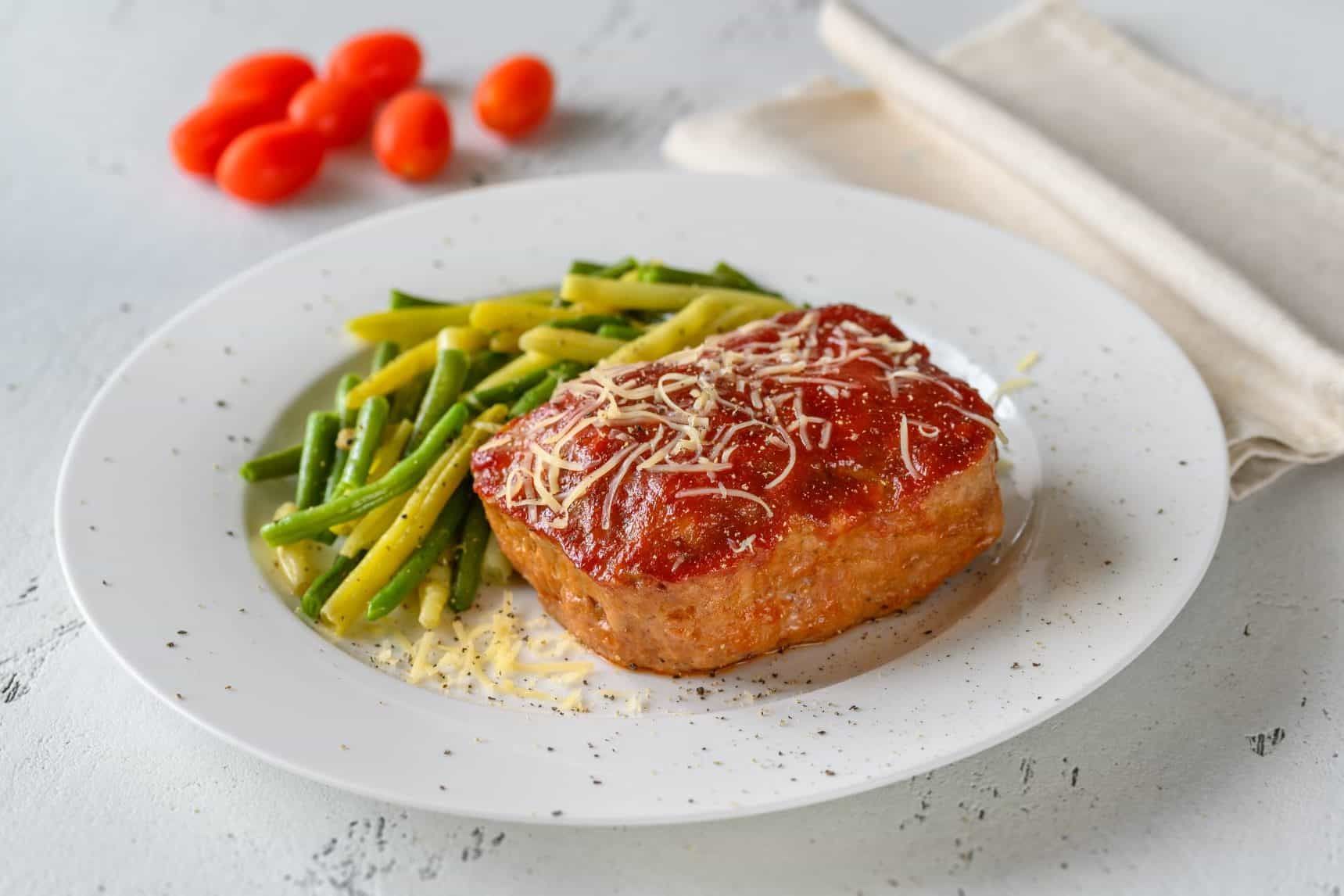 A white plate topped with a piece of meat and green beans.