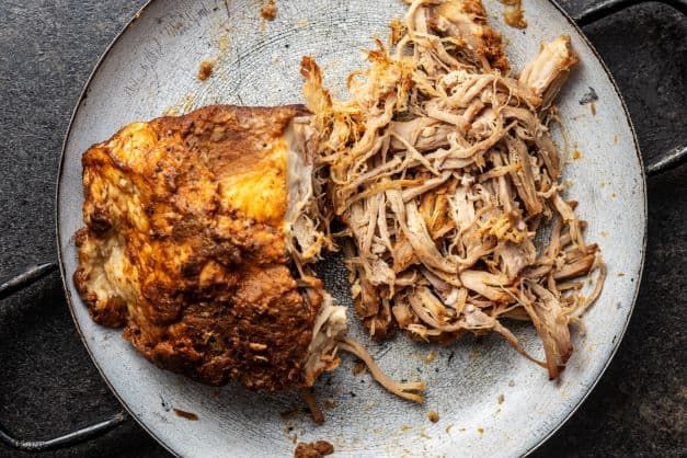 A plate of pulled pork and a piece of chicken on a table.