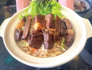 A bowl of food with meat and rice on a table.