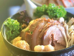 A bowl of food with meat and vegetables on a table.