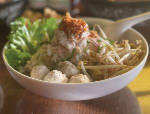 A bowl of food with noodles , meatballs and vegetables on a table.