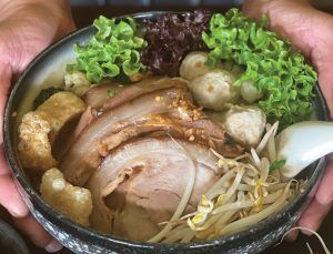 A person is holding a bowl of soup with meat and vegetables.