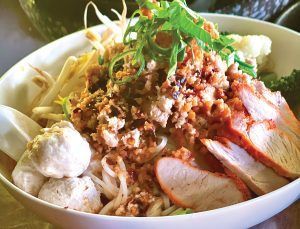 A bowl of food with meat and noodles on a table.