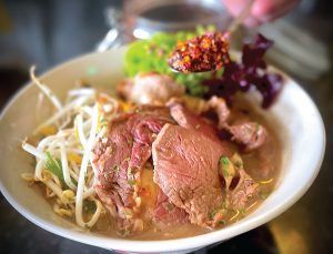 A person is holding a bowl of soup with meat and noodles.