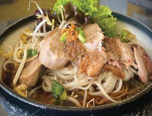 A bowl of noodles with meat and vegetables on a table.