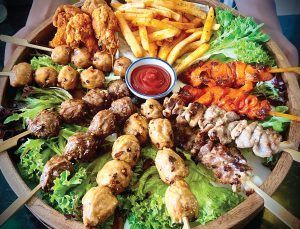 A wooden tray filled with a variety of skewers and french fries.