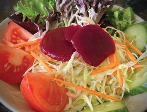 A close up of a salad with tomatoes , cabbage , carrots and beets on a plate.