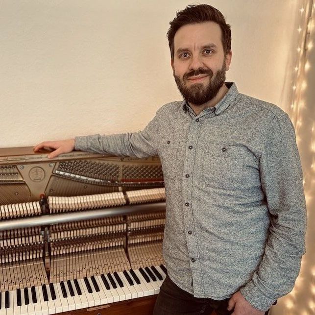 Max-Ole Tammen steht neben einem Klavier und schaut in die Kamera