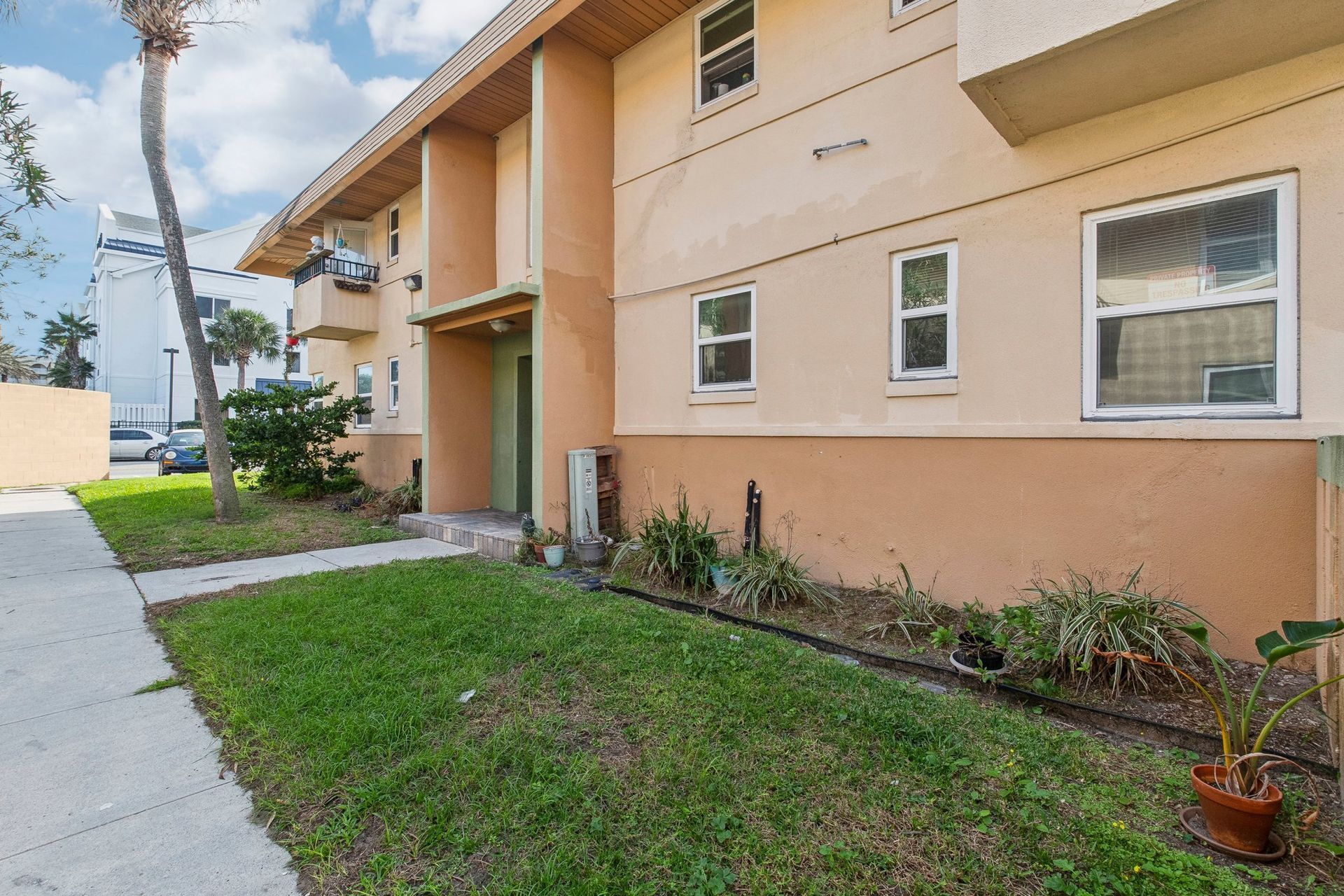 Tan apartment building with green lawn and sidewalk.