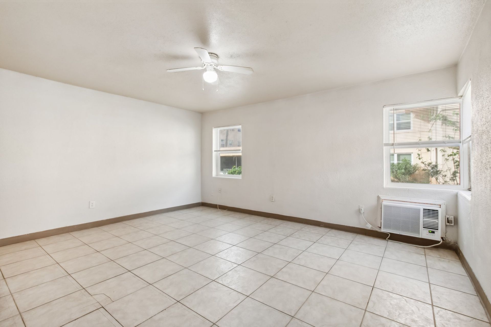 Empty, white-walled room with tile floor, windows, and an air conditioning unit.