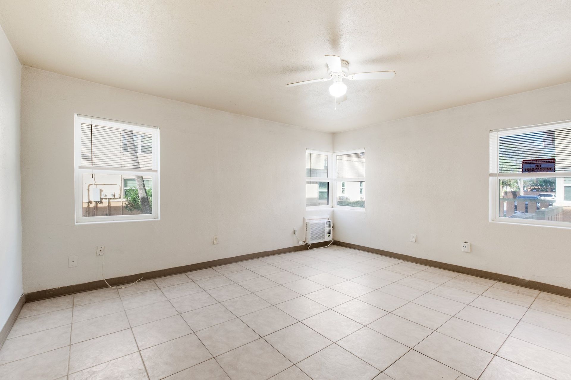 Empty room with tiled floor, three windows with blinds, ceiling fan.