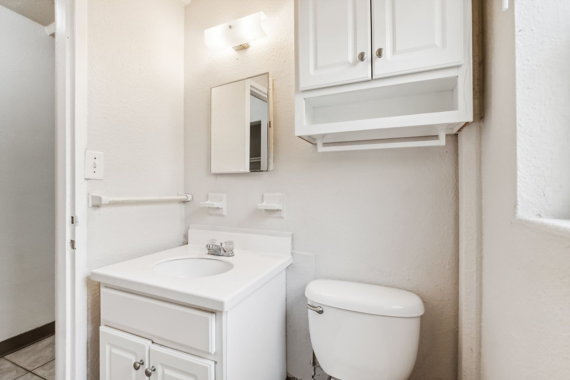 White bathroom with a vanity, toilet, mirror, and cabinet.
