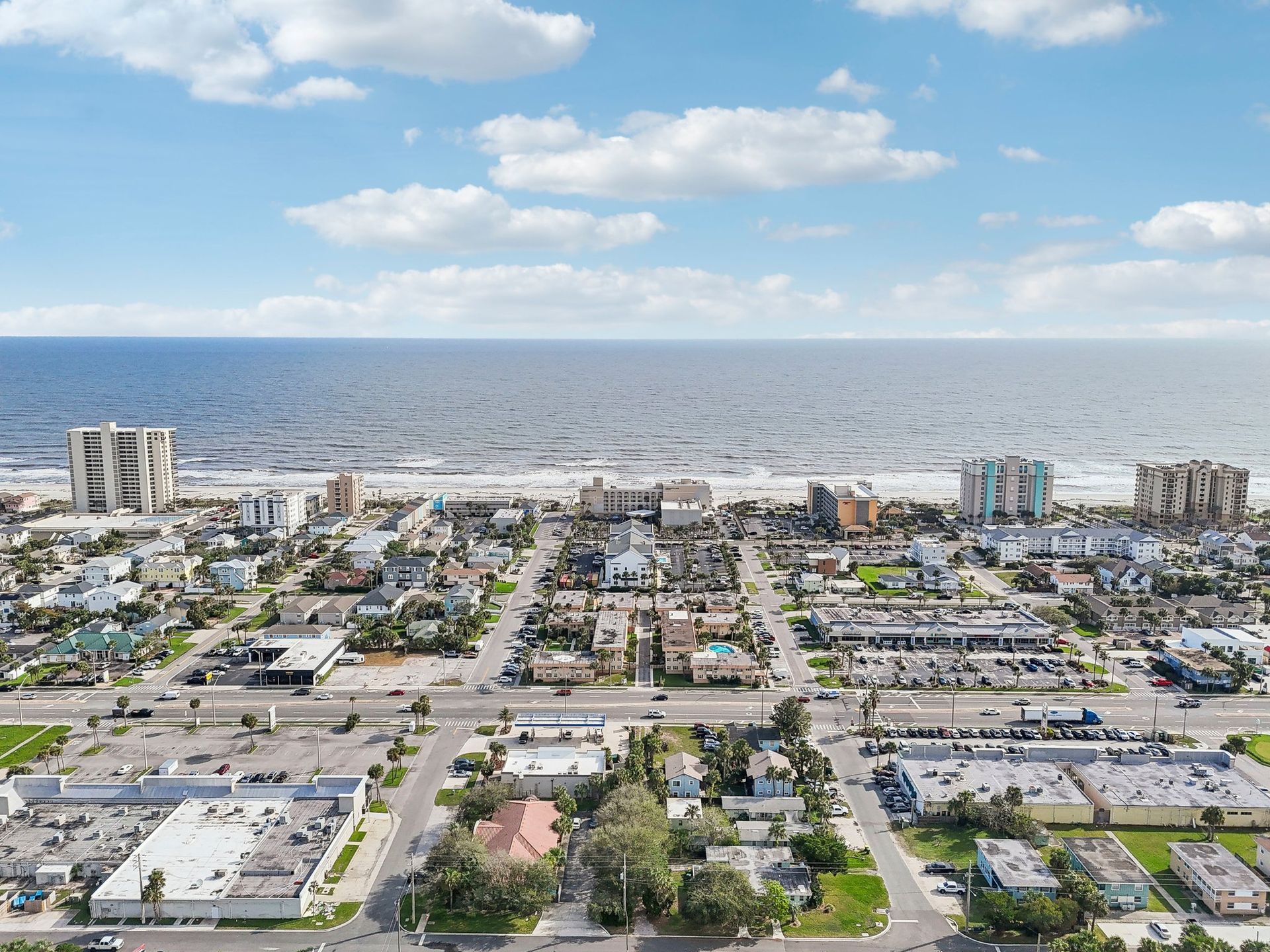 Aerial view of a coastal town with buildings, streets, and the ocean under a cloudy sky.